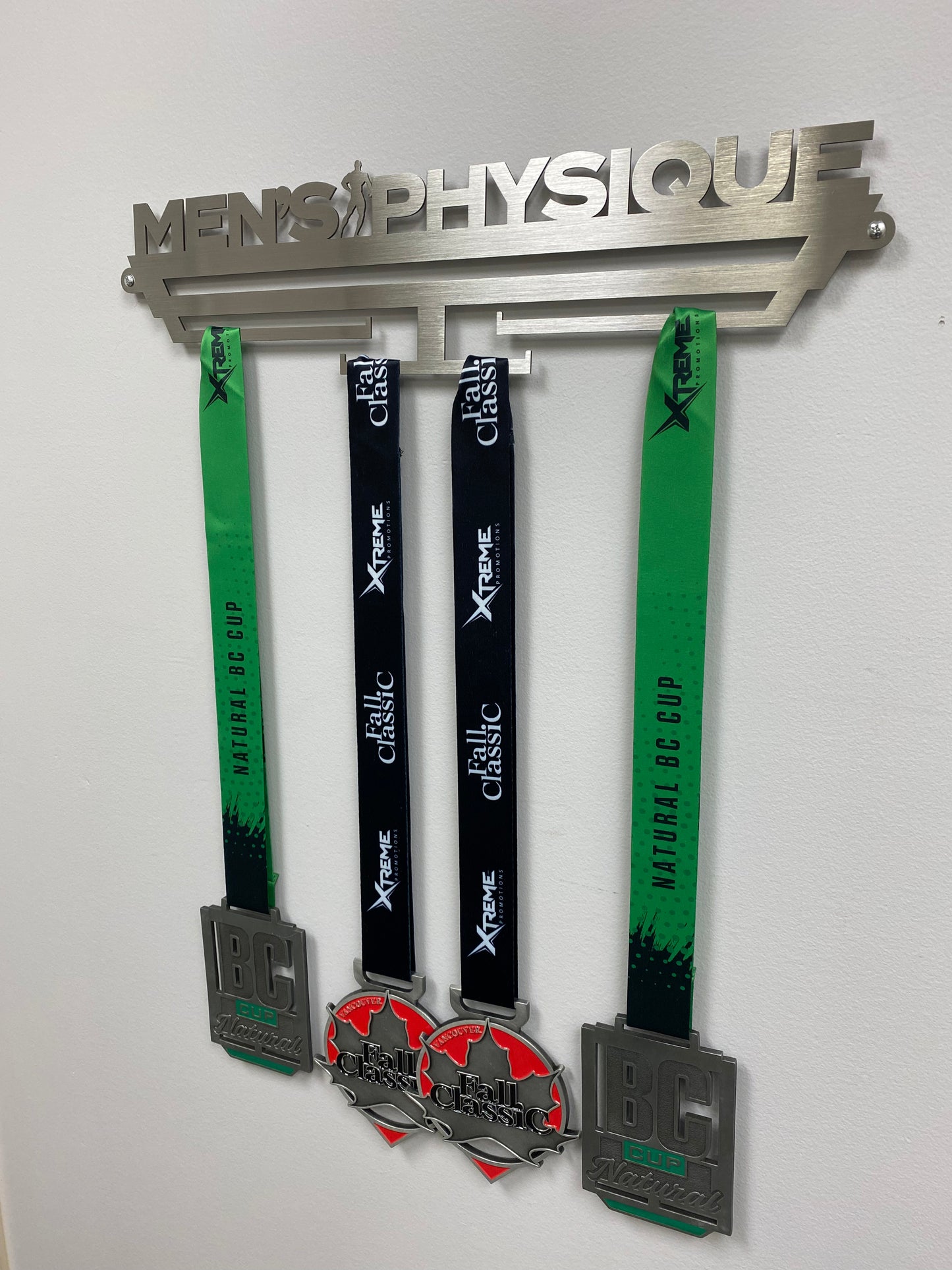 medal hanger for medallions, it reads Men’s Physique across the top and has a Physique competitor posing in between the word men’s and Physique and has 4 bars that you can hang the lanyards off of that will display the medals. You will mount this to a wall with the screw kit provided.